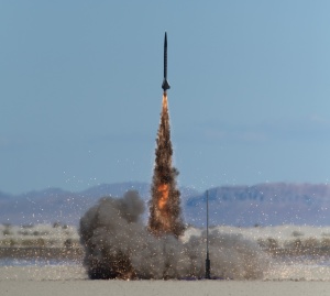 A rocket launches on a large skidmark motor producing black smoke and golden sparks